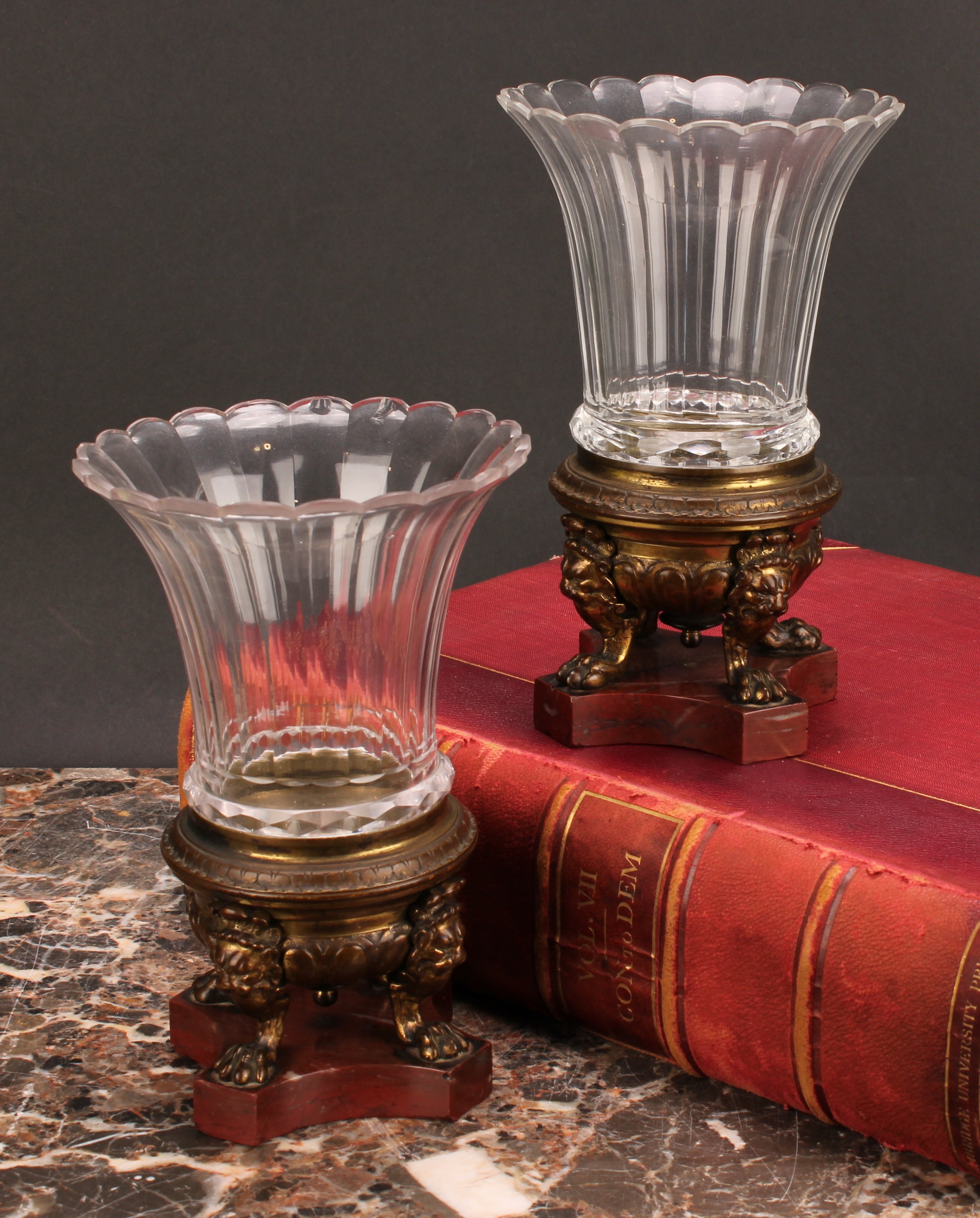 A 19th century pair of gilt bronze and clear glass mantel urns, cast lion monopodia, incurved canted