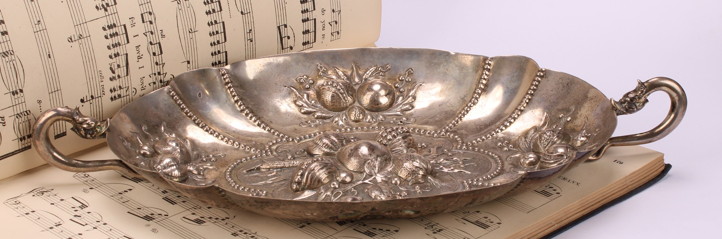 A German silver shaped oval fruit dish, chased in bold relief with leaves and ripe fruit, rustic