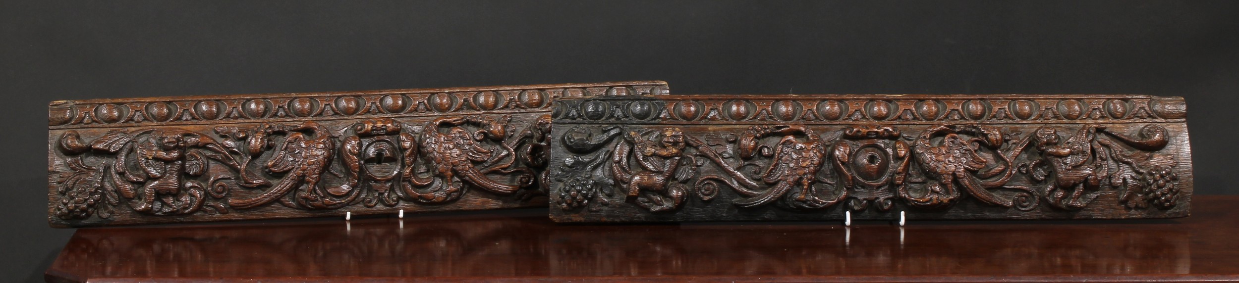 A pair of 17th century oak rectangular panels, each carved with birds, fruiting foliage and putti