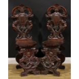 A pair of 19th century Italian walnut sgabelli or hall chairs, carved throughout in the