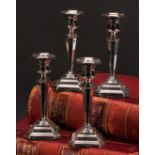 A composed set of four George V silver candlesticks, octagonal sconces, tapered pillars, canted