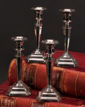 A composed set of four George V silver candlesticks, octagonal sconces, tapered pillars, canted