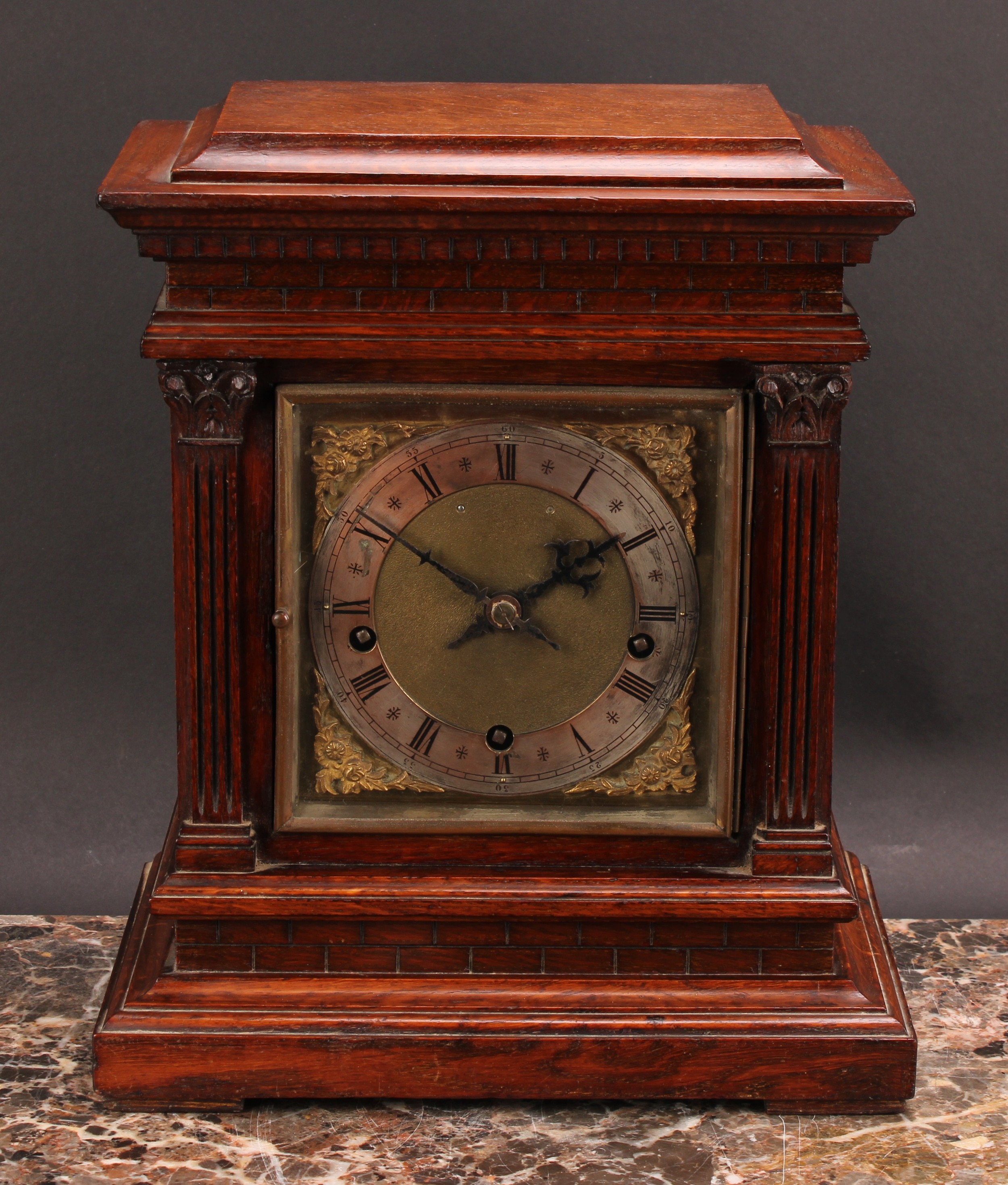 An early 20th century oak architectural bracket-form mantel clock, 15cm square brass dial with