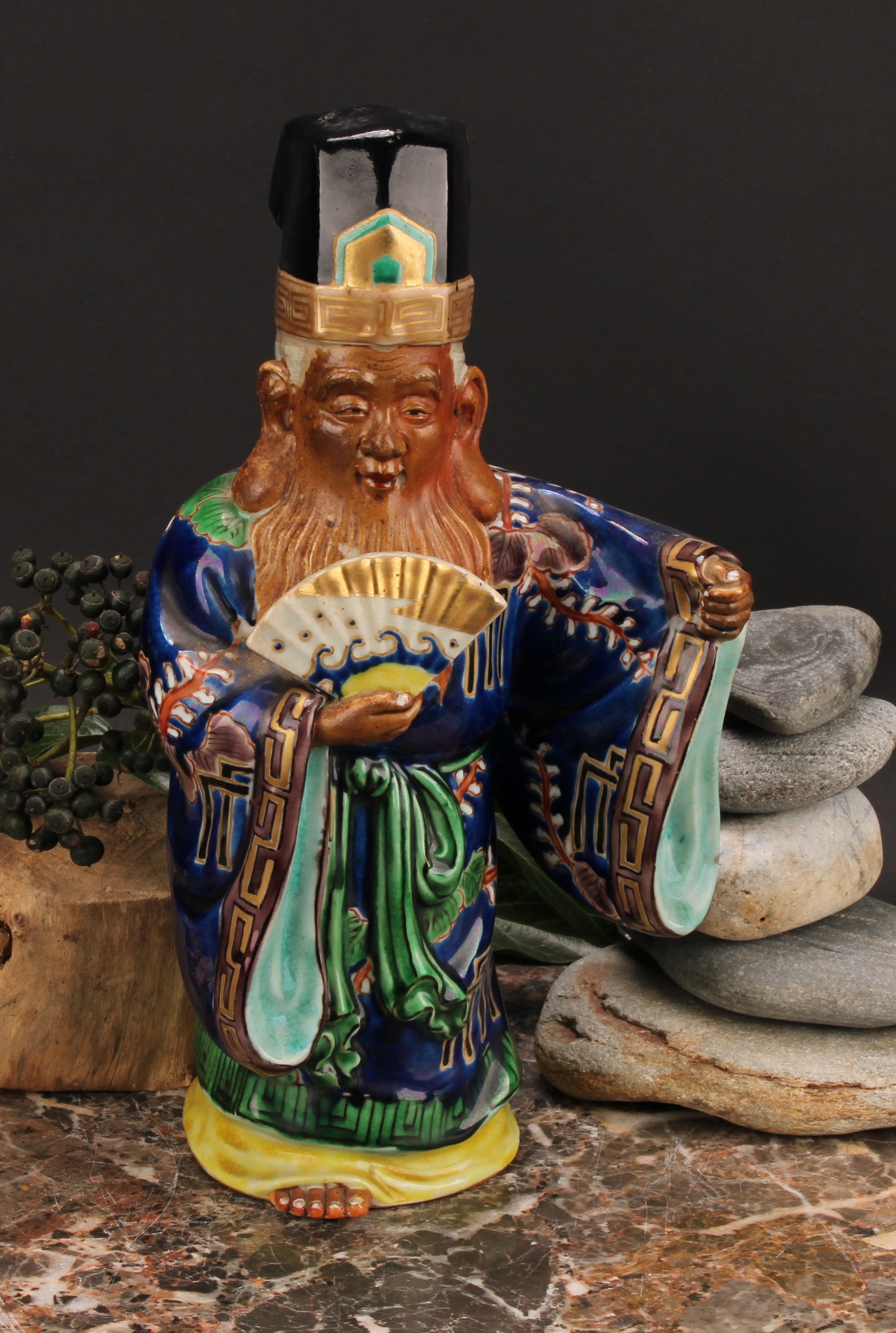 A Japanese porcelain figure, of an elder holding a fan, painted in polychrome and picked out in