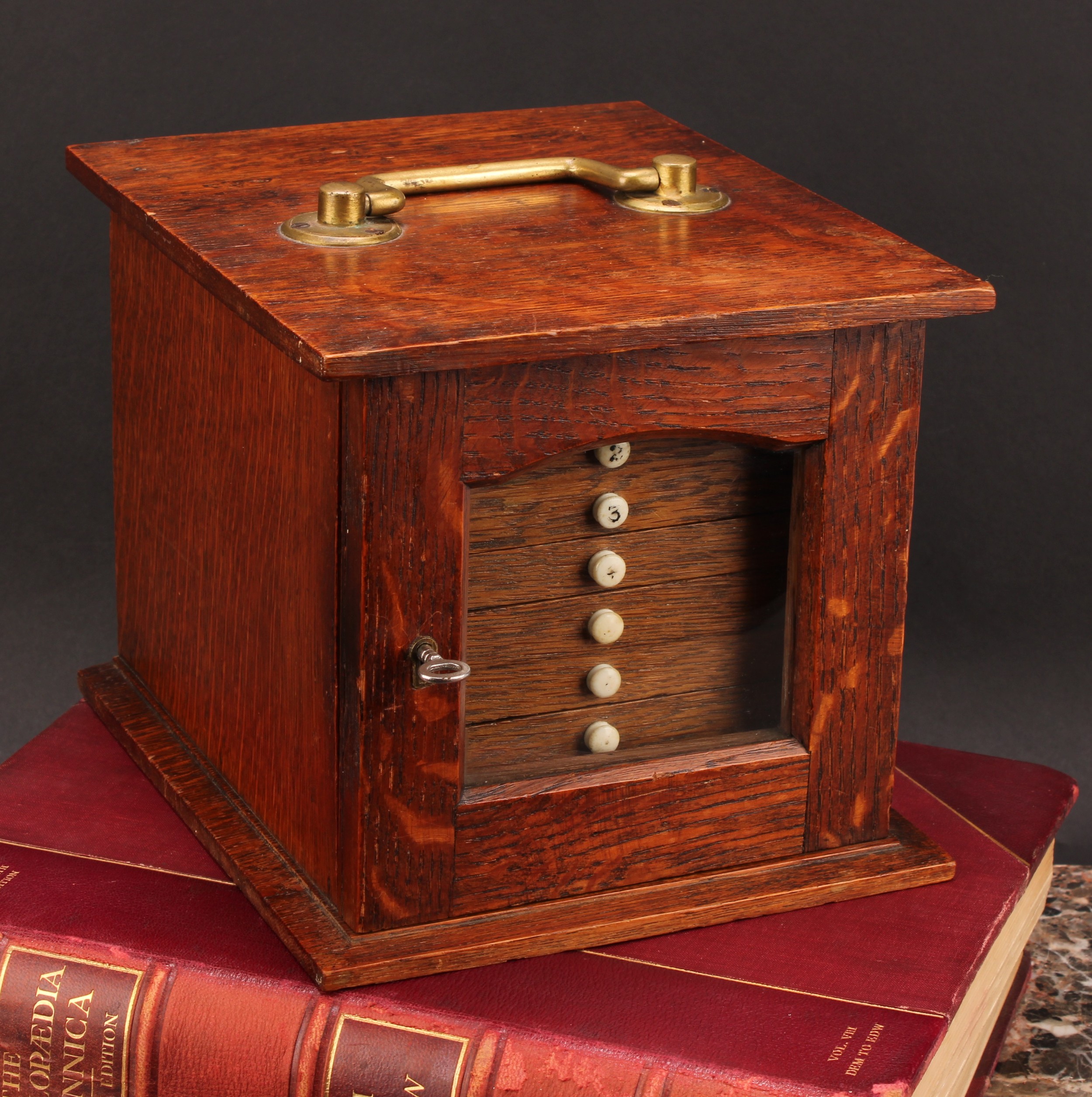 Numismatics - An Edwardian Arts and Crafts oak coin cabinet, the oversailing rectangular top with