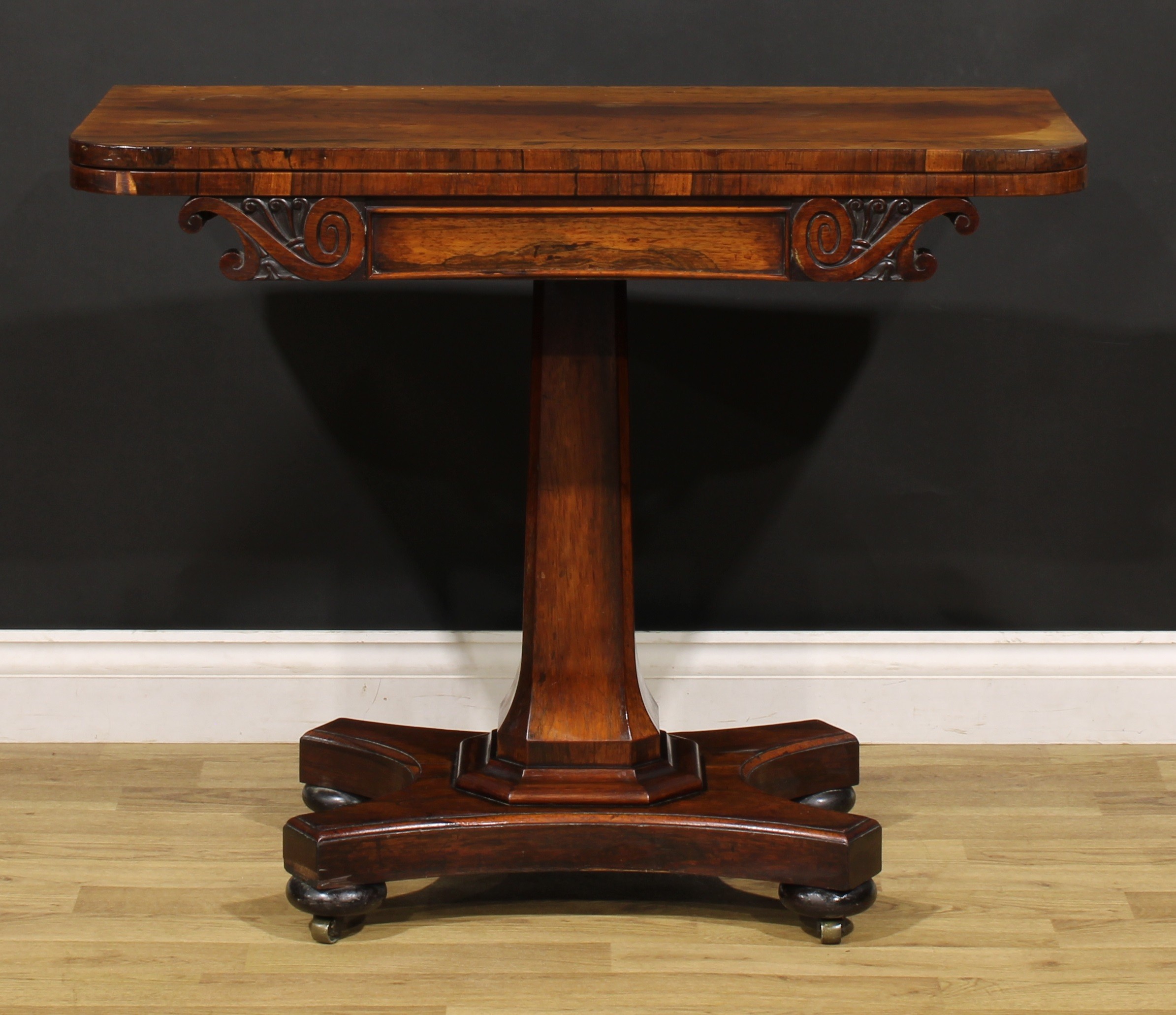 A William IV rosewood card table, rounded rectangular folding top above a frieze carved with leafy