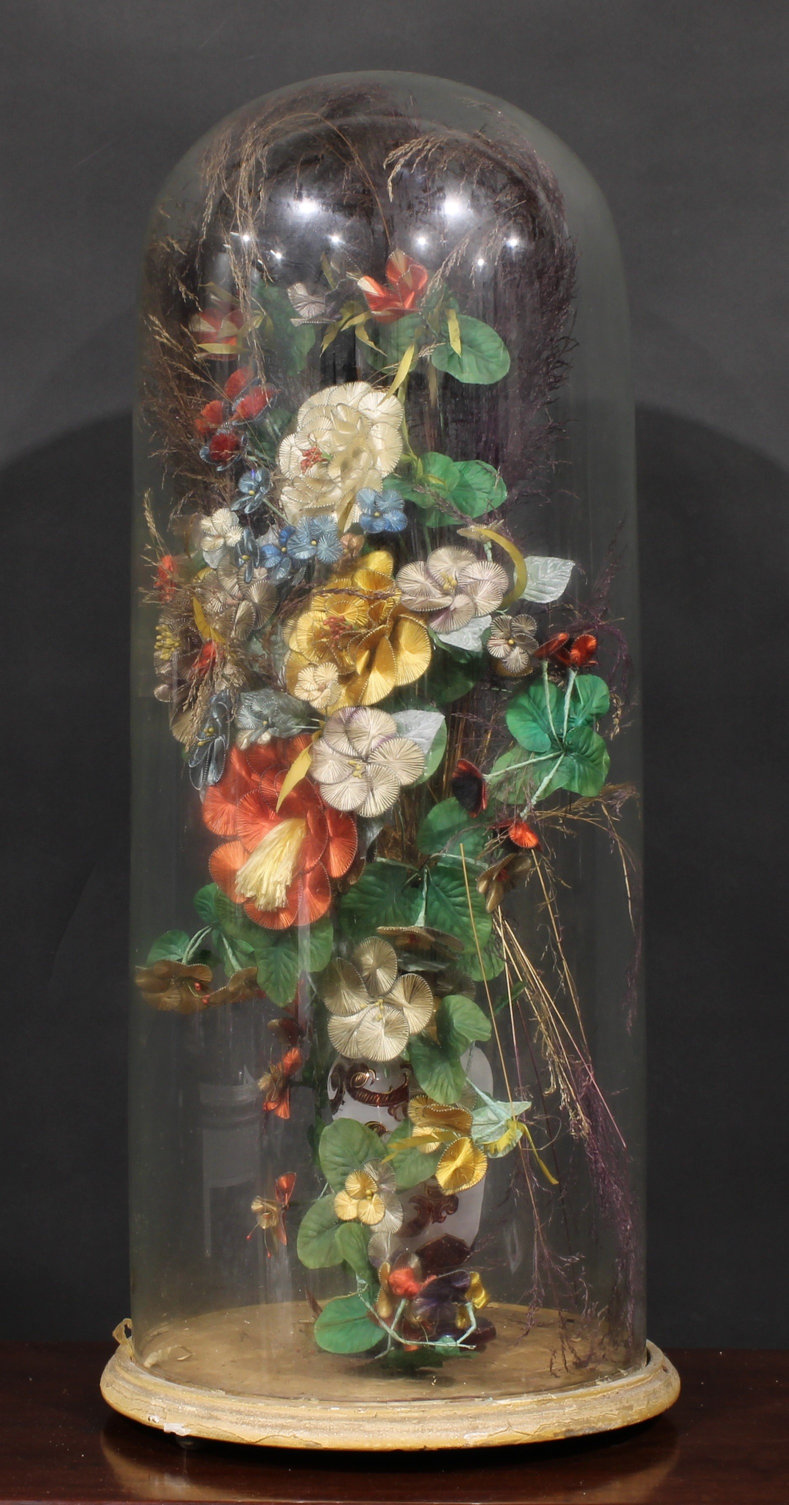 A large Victorian glass dome, enclosing an arrangement of faux flowers, grasses and leaves, in a - Image 2 of 2