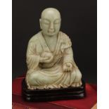 A Chinese soapstone figure, carved as a Buddhist disciple, or Luohan, holding a peach, 21cm high,