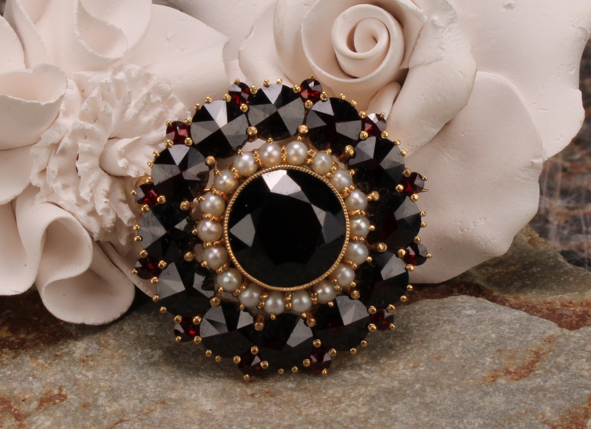 A Victorian style garnet and seed pearl target brooch, the large central round facet cut stone