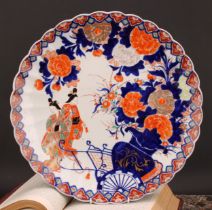 A Japanese scalloped circular charger, painted in the Imari palette with floral vase, rickshaw and
