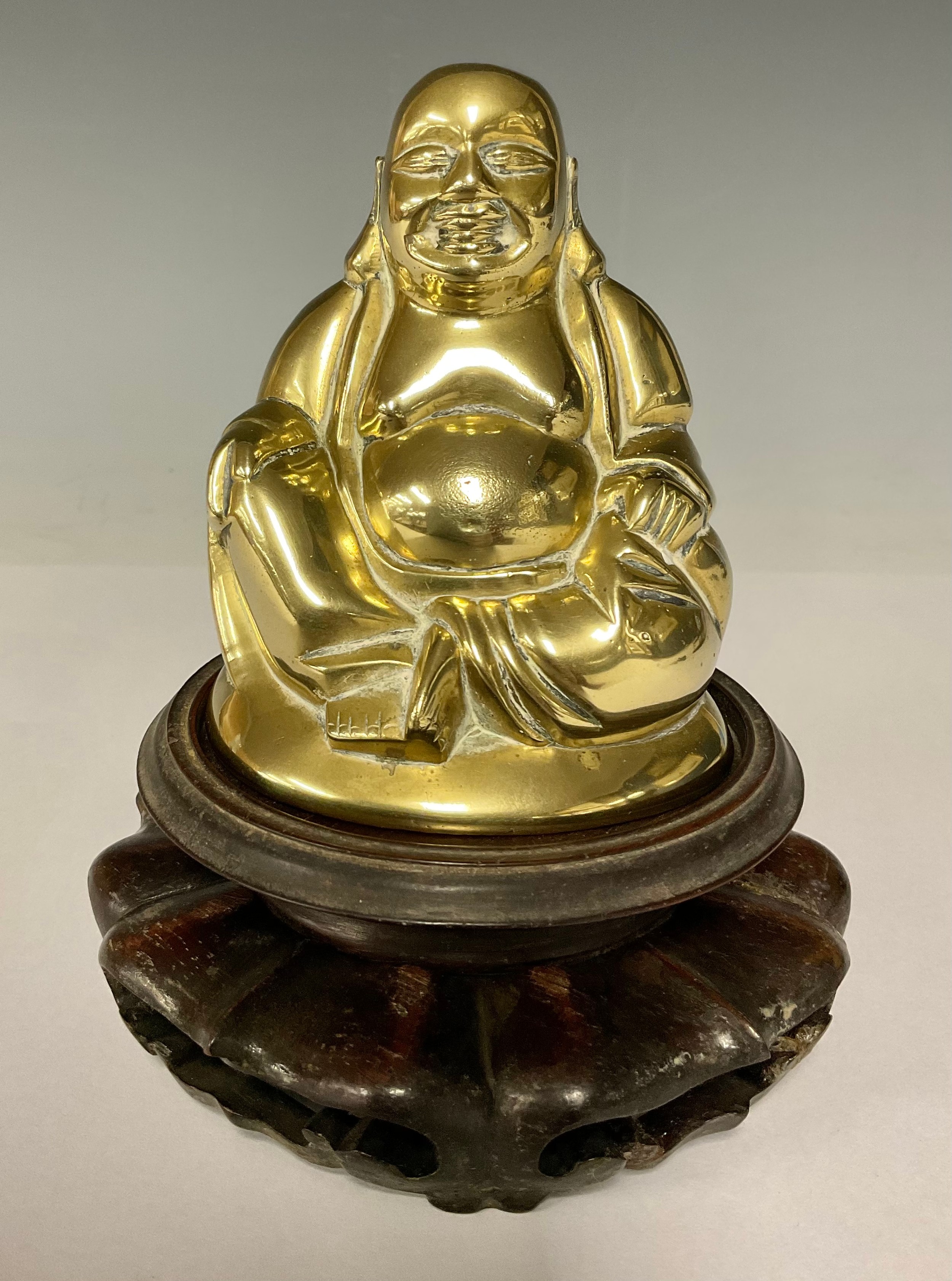 A brass seated laughing Buddha figure, 11cm, pierced circular hardwood stand
