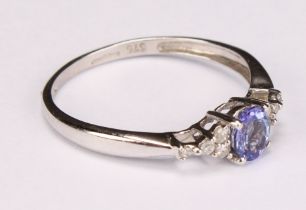 A tanzanite and white sapphire ring, the central blue oval facet cut stone flanked by 8 small