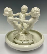 A German Hutschenreuther porcelain table centre, as three putti dancing in a circle, the circular