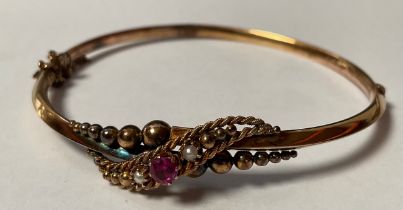 An Edwardian 9ct gold hinged bangle, set with seed pearl and ruby stones, marked 9ct, safety