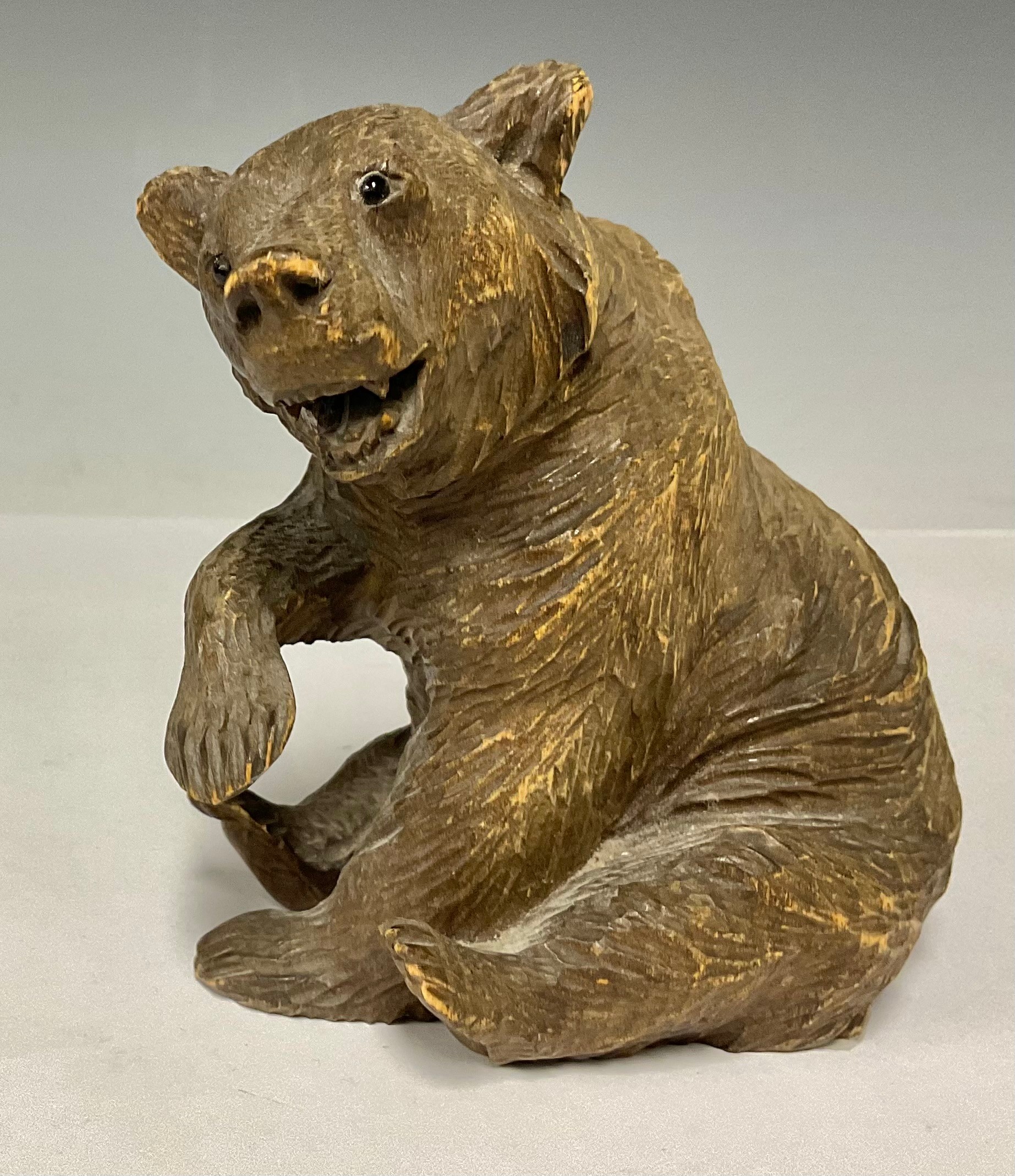 A German Black Forest carved wooden bear, seated, glass eyes, 11.5cm, c.1900