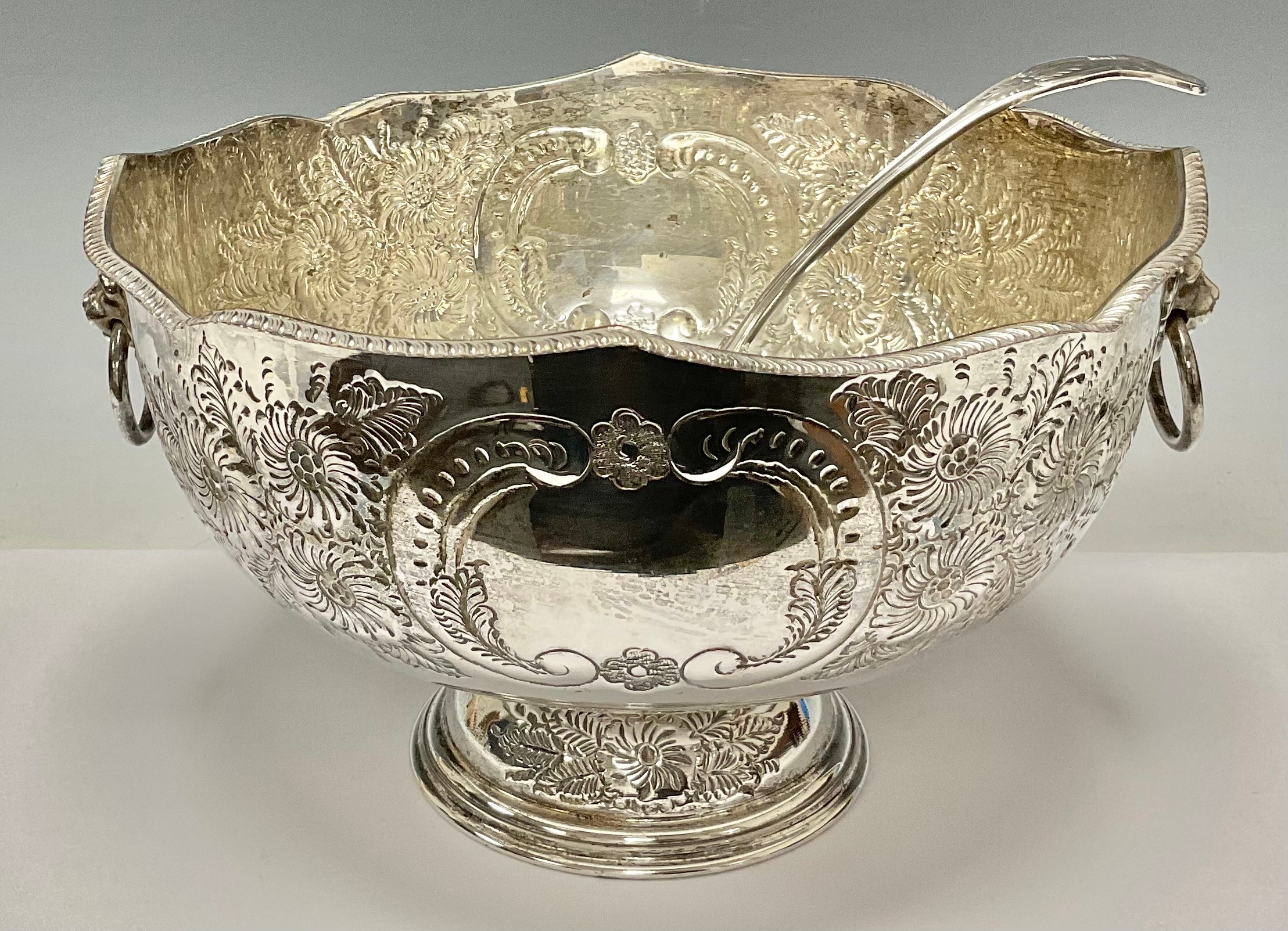 A large silver plated pedestal punch bowl, embossed with foliate scrolls, pair of lion mask loop