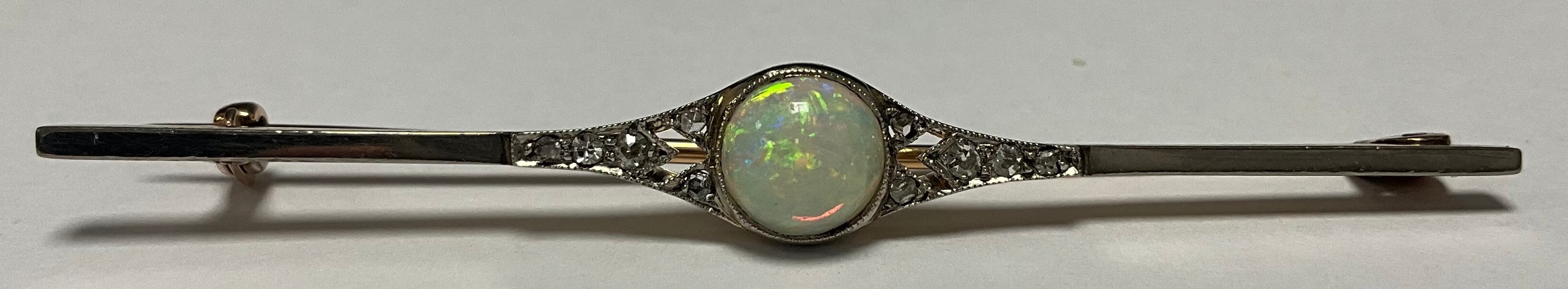 A gold bar brooch, unmarked, set with a single circular polished opal cabochon, flanked by five