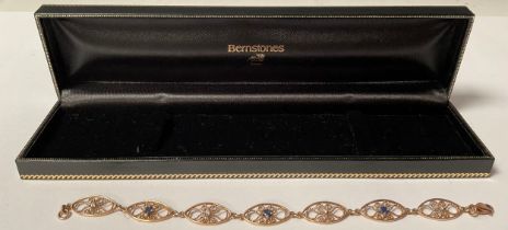 An unmarked gold openwork filigree bracelet, the seven oval links set alternately with sapphire