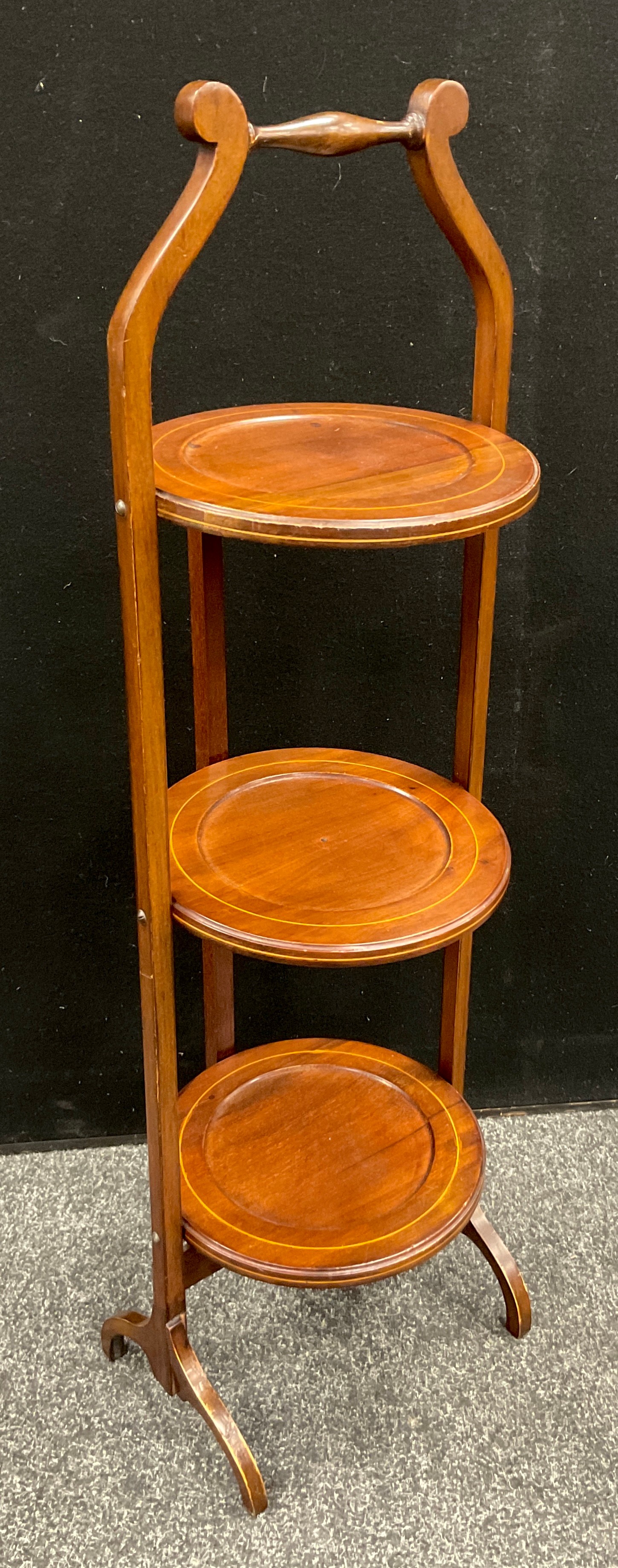 An Edwardian mahogany three tier folding cake stand, outlined with boxwood stringing, c.,1905