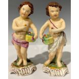 A pair of 19th century Staffordshire figures, each as putti with baskets of fruit, in polychrome,