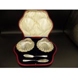 A pair of cased silver scallop shell shaped butter dishes and knives. Hallmarked - Sheffield 1901 by