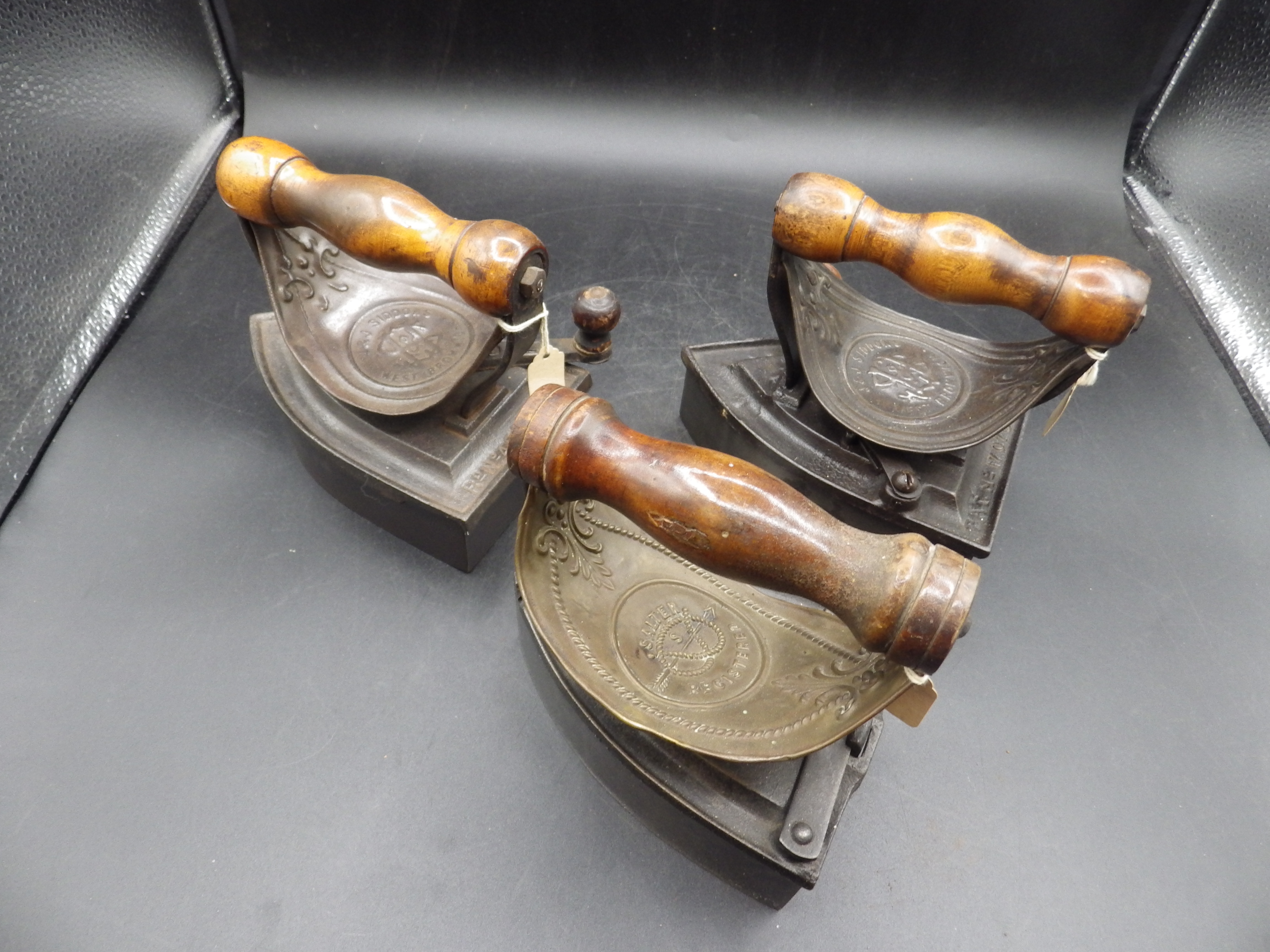 3 box irons with brass? heat shields and wooden handles together with slugs to incl 2x J & J Siddons