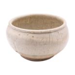 A Chinese cream glazed bowl with rolled rim, the thick glaze falling short of the foot,