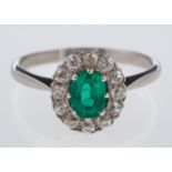 An emerald & diamond ring, the oval emerald of fine colour, within a border of old cut diamonds,