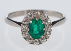An emerald & diamond ring, the oval emerald of fine colour, within a border of old cut diamonds,
