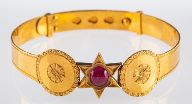 A gold bangle with a cabochon ruby in star setting bordered by floral engraved decoration, ruby 7.