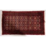 An Afghan Balouch rug, the red striped field with three rows of hooked lozenge medallions,