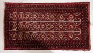 An Afghan Balouch rug, the red striped field with three rows of hooked lozenge medallions,