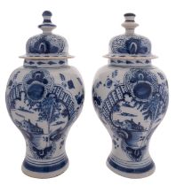 A pair of Dutch Delft blue and white baluster vases and covers each painted with buildings by a
