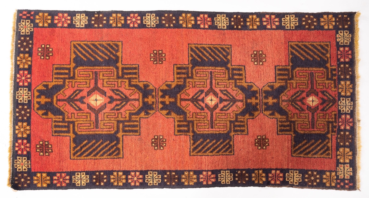 An Afghan rug, the brick red field with triple stepped and shaded geometric medallions,