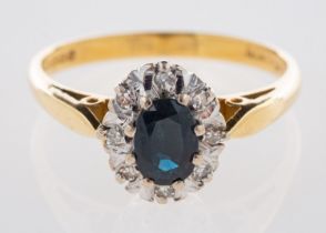 An 18ct yellow gold cluster ring, set centrally with an oval-cut dark blue sapphire,