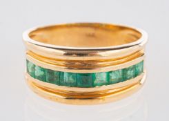An emerald ring, a wide band set to the centre with a row of nine table-cut emeralds, marked 14k,