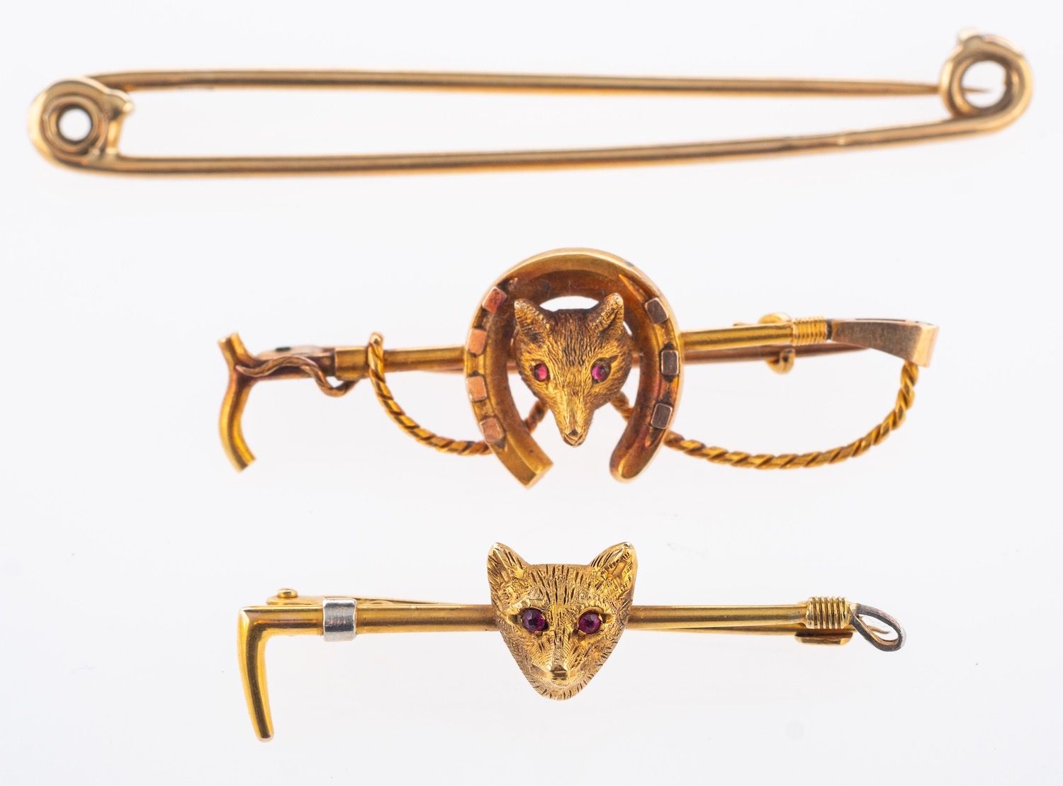 A group of three brooches, including a fox head, horseshoe & riding crop brooch, marked 15ct,