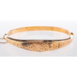 A 9ct yellow gold bangle, with flower and foliate engraving to the front section, (dented), hinged,