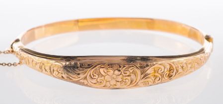 A 9ct yellow gold bangle, with flower and foliate engraving to the front section, (dented), hinged,