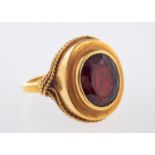 An 18ct yellow gold ring set with an oval-cut garnet in a collet and rope twist setting, size O 1/2,