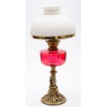 A late Victorian brass oil lamp with reeded opaque white glass shade and cranberry glass circular