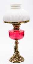 A late Victorian brass oil lamp with reeded opaque white glass shade and cranberry glass circular