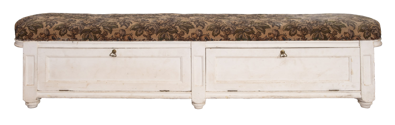 A cream painted ottoman window seat with upholstered tapestry top and two hinged flaps to the