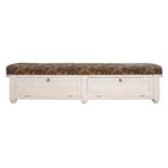 A cream painted ottoman window seat with upholstered tapestry top and two hinged flaps to the