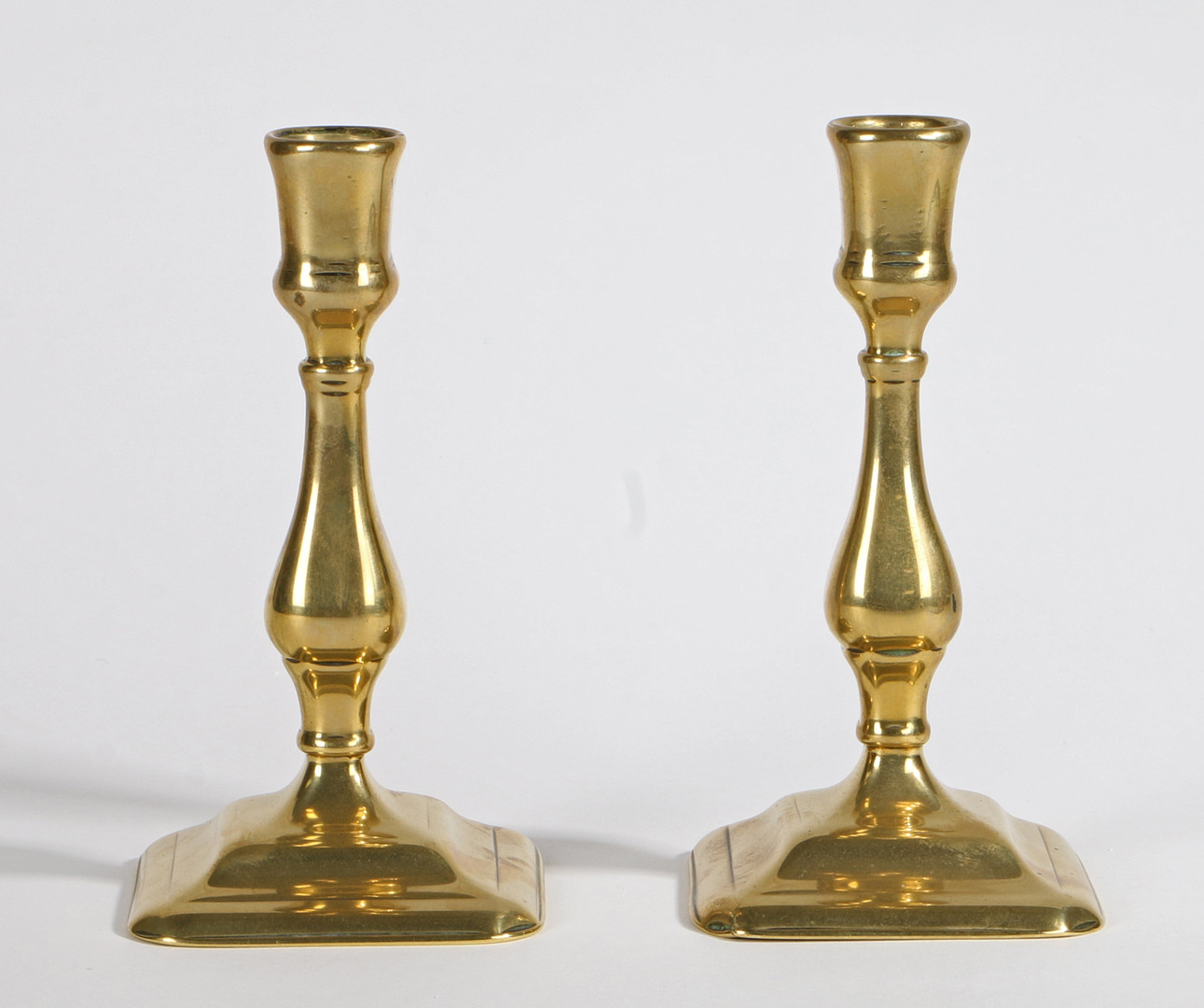 A PAIR OF GEORGE II BRASS SQUARE-BASE CANDLESTICKS, CIRCA 1730.