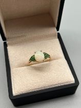 10ct yellow gold ring set with an oval cut opal stone flanked by green tourmaline stones. [Ring size