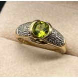 9ct yellow gold ring set with a round cut green tourmaline and diamond cluster shoulder. [Ring