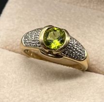 9ct yellow gold ring set with a round cut green tourmaline and diamond cluster shoulder. [Ring