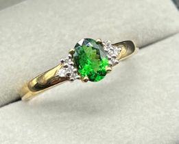 10ct yellow gold ring fitted with an oval cut emerald off set by round cut white topaz stones to the