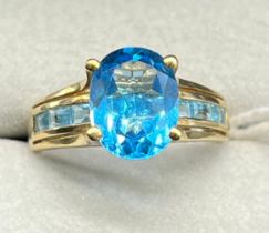 9ct yellow gold ring set with an oval cut blue topaz and emerald cut blue topaz gem stones. [Ring